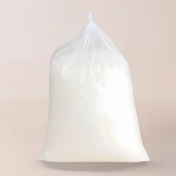 Una bolsa de plástico transparente llena de cera de soja, una sustancia en polvo blanca ideal para hacer velas, se encuentra en posición vertical sobre un fondo liso y neutro.