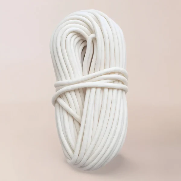 Un trozo enrollado de Pabilo Importado, de color blanco y comúnmente utilizado como insumo para velas, está cuidadosamente envuelto y en posición vertical sobre un fondo sencillo y claro.