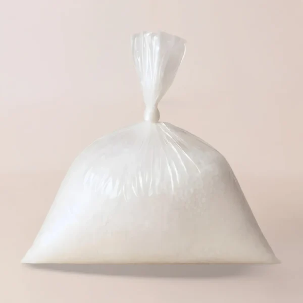 Una bolsa de plástico transparente llena de gránulos de aditivo Vybar blanco, ideales como insumos para velas, está atada en la parte superior sobre un fondo claro y liso.