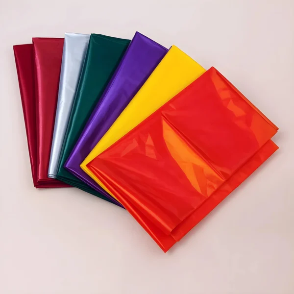 Seis láminas de Celofán Frío en colores rojo, plateado, verde, morado, amarillo y naranja se extienden en abanico sobre una superficie clara: insumos ideales para velas para fabricantes y artesanos de Velas Colombia.